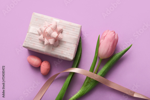 Easter eggs with tulip flower and gift box on purple background