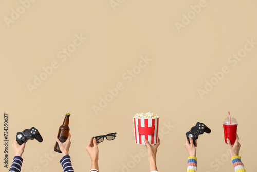 Many hands with bucket of popcorn, drinks and game pads on beige background