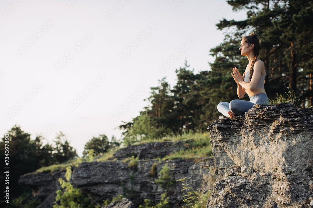 A young woman practices yoga and meditates in the mountains at sunset. Peace and unity with nature.