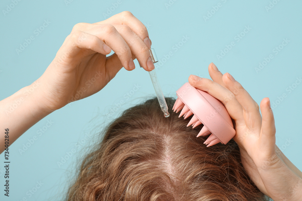 Naklejka premium Young woman using hair scalp massager with cosmetic oil on blue background, closeup