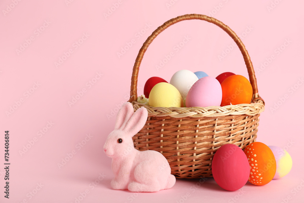 Wicker basket with painted Easter eggs and bunny on pink background