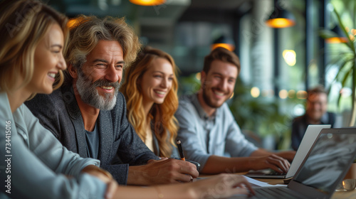  Smiling businesspeople having a discussion while collaborating on a new project in an office. Group of happy businesspeople using a laptop while working together in a modern workspace in the office