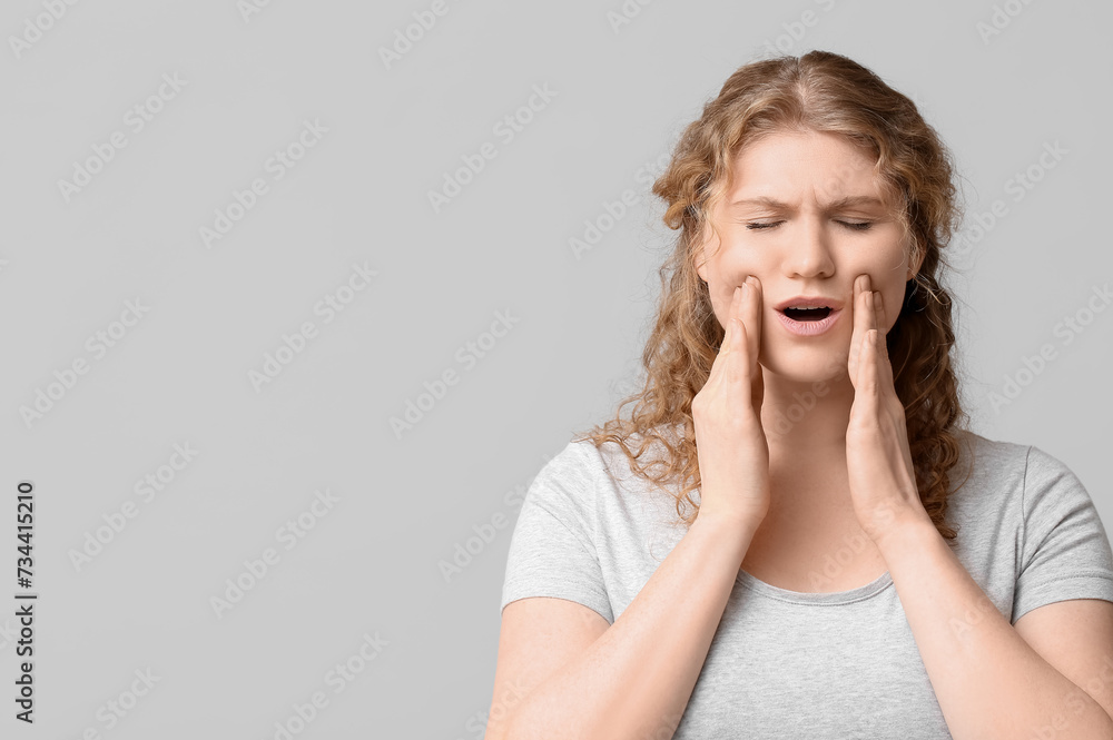 Beautiful young woman suffering from toothache on grey background Beautiful young woman suffering from toothache on grey background