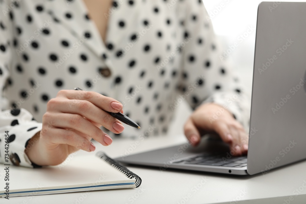 Fototapeta premium E-learning. Woman taking notes during online lesson at table indoors, closeup