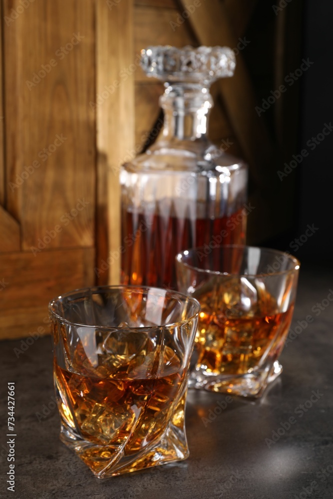 Whiskey with ice cubes in glasses and bottle on grey table Whiskey with ice cubes in glasses and bottle on grey table