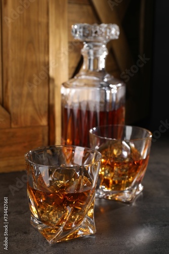 Whiskey with ice cubes in glasses and bottle on grey table