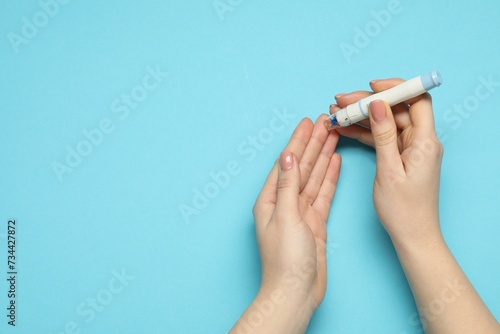 Diabetes. glucose testing. Woman using lancet pen on blue background, top view. Space for text © New Africa