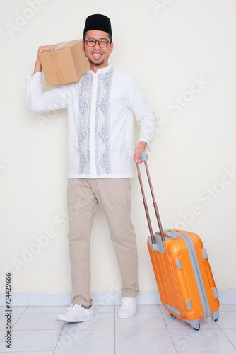 Full body portrait of moslem man pulling suitcase and carrying a package cardboard photo