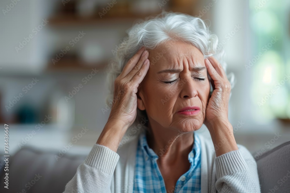 A lady's weary expression is highlighted by the wrinkles on her skin as she holds her head in contemplation, standing against a plain wall in her indoor surroundings, wearing clothing and clutching a A lady's weary expression is highlighted by the wrinkles on her skin as she holds her head in contemplation, standing against a plain wall in her indoor surroundings, wearing clothing and clutching a