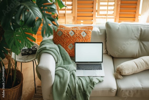 A cozy indoor setting with a houseplant and flowerpot on a windowsill, a laptop resting on a pillow on the couch, while the warm light from the window illuminates the room