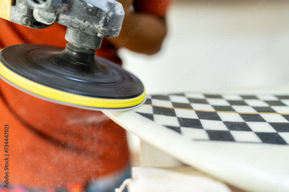 Close-up of a worker polishing a surfboard in a workshop Close-up of a worker polishing a surfboard in a workshop
