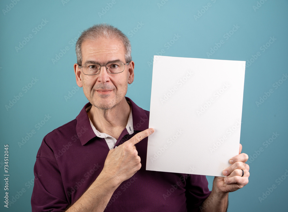 Sixty-year-old man holds up a blank white sign with room for copy and points to it Sixty-year-old man holds up a blank white sign with room for copy and points to it