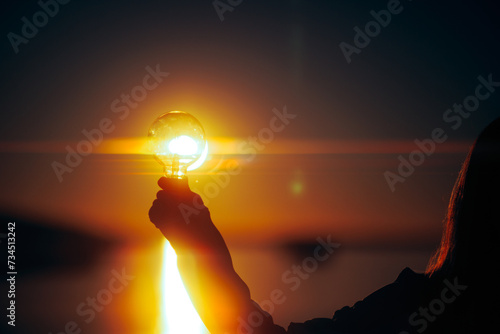 Person Holding a Light bulb Full of Solar Energy in the Sunset. Eco-friendly solution for alternative energy concept image 