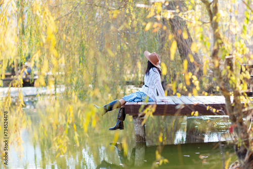 Autumn lake woman. She sits by a pond on a wooden pier in autumn and admires nature. The concept of tourism, weekends outside the city.