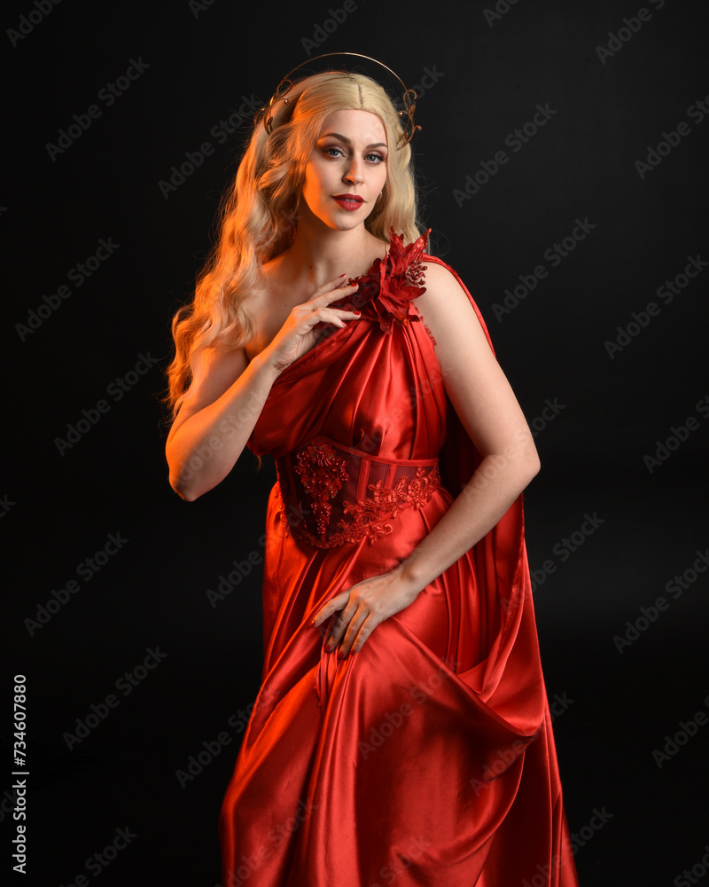 Close up portrait of beautiful blonde model wearing flowing red silk toga gown and crown, dressed as ancient mythological fantasy goddess. Graceful elegant pose isolated on dark studio background. Close up portrait of beautiful blonde model wearing flowing red silk toga gown and crown, dressed as ancient mythological fantasy goddess. Graceful elegant pose isolated on dark studio background.