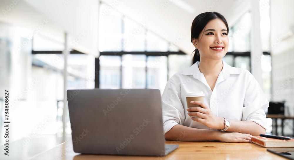 Image of young beautiful joyful woman smiling and relaxing while working with laptop in office Image of young beautiful joyful woman smiling and relaxing while working with laptop in office