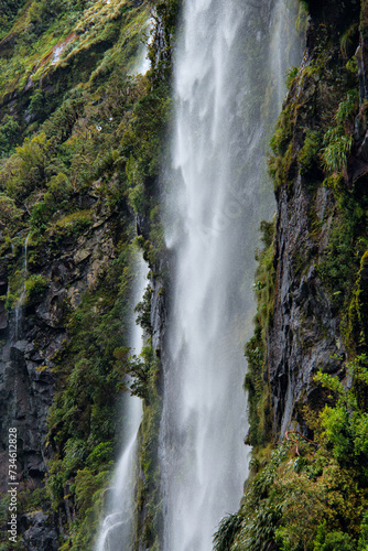 Milford Sound's cascading waterfall, a breathtaking spectacle amidst lush greenery. Majestic, serene, iconic, scenic, Fiordland, nature, New Zealand. © OzCam