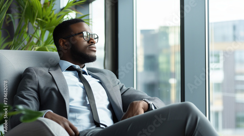 Confident serious focused stylish rich african black man sitting in chair at home looking away through window dreaming thinking of success, leadership, business vision, planning future in luxury life. photo