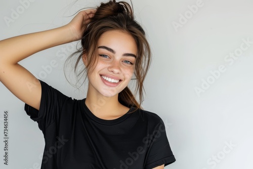 A lovely young woman appears cheerful and stylish as she smiles and poses for a portrait She sits alone on a white background in a black t shirt gently running h © LimeSky