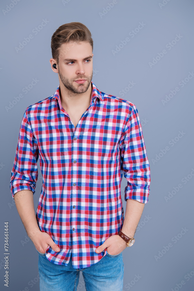 Millennial man using wireless gadget of handsfree headset or earphones device isolated on grey Millennial man using wireless gadget of handsfree headset or earphones device isolated on grey