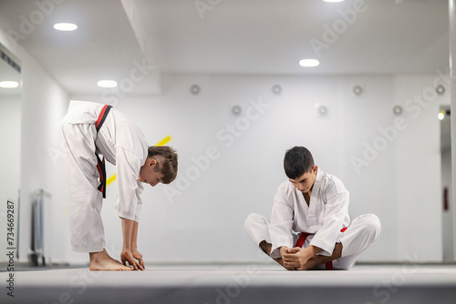 Taekwondo boys in kimonos practicing flexibility at martial art school.