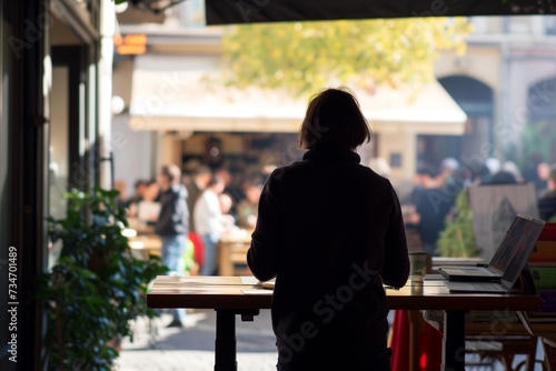 person at standing desk watches bustling outdoor caf