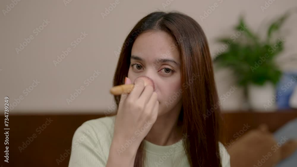 Woman sits looks in mirror apply makeup, woman holding facial brush swipe beautiful face, add color make face look more beautiful, look closely at mirror, use fingers spread it on beautiful face. Woman sits looks in mirror apply makeup, woman holding facial brush swipe beautiful face, add color make face look more beautiful, look closely at mirror, use fingers spread it on beautiful face.