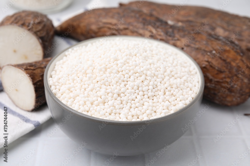 Tapioca pearls in bowl and cassava roots on white tiled table, closeup Tapioca pearls in bowl and cassava roots on white tiled table, closeup