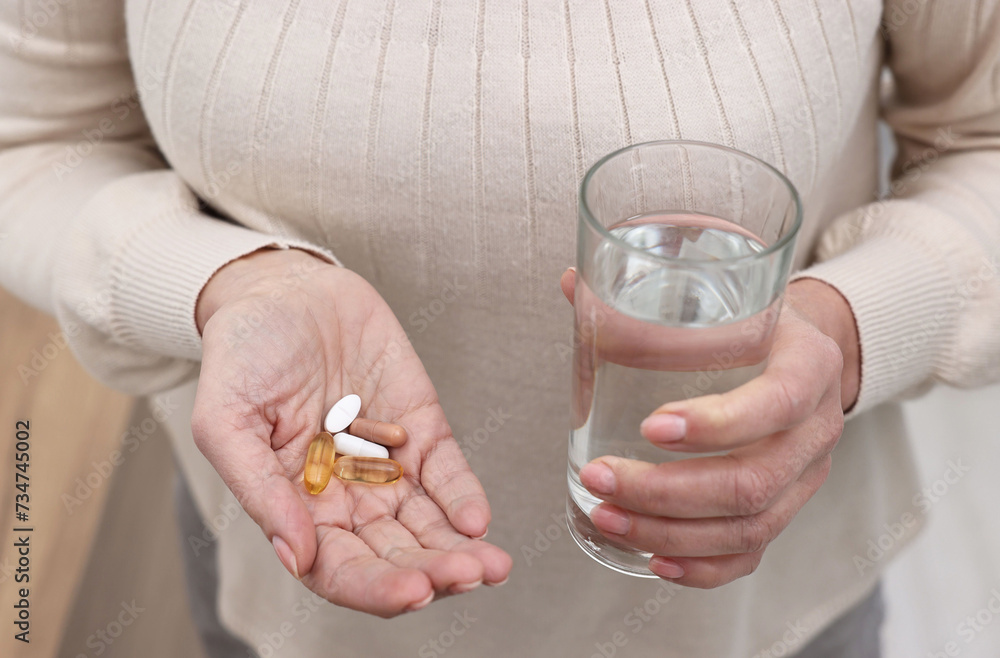 Woman with vitamin pills and glass of water indoors, closeup Woman with vitamin pills and glass of water indoors, closeup