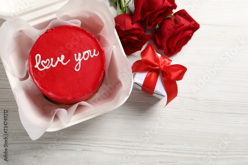 Bento cake with Love You text in takeaway packaging, roses and gift box on white wooden table, top view. St. Valentine's day surprise