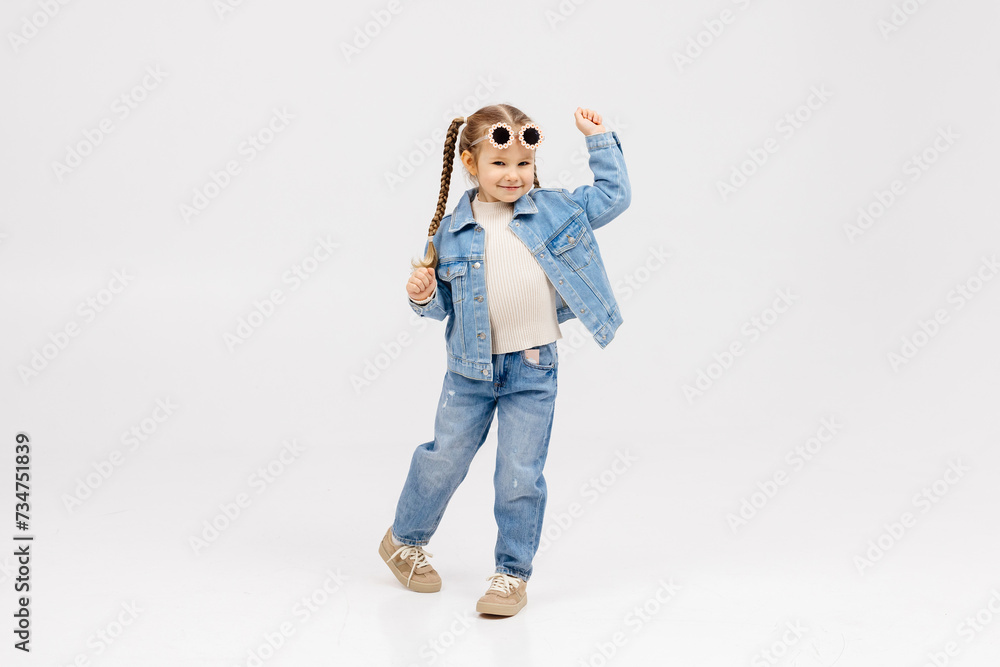 Cheerful little girl in modern clothes having fun, performing freestyle dance moves, on isolated white background. Children's clothing advertising concept Cheerful little girl in modern clothes having fun, performing freestyle dance moves, on isolated white background. Children's clothing advertising concept