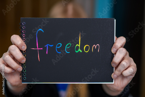 Kolorowy napis freedom napisany na kartce i trzymany w dłoni przez kobietę 