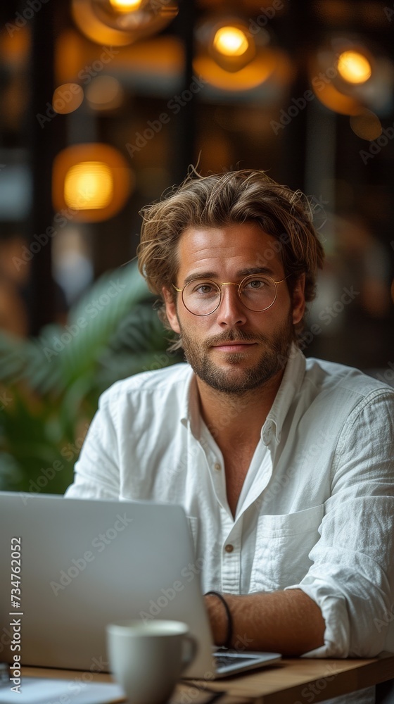 Man with beard and glasses sitting at table with laptop in cafe, warm lighting overhead, generative ai Man with beard and glasses sitting at table with laptop in cafe, warm lighting overhead, generative ai