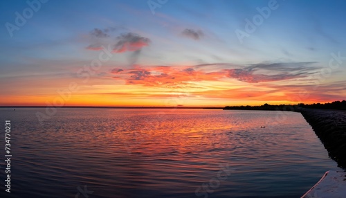 A wide-angle image of the sunset beyond the bay in Delaware showing dynamic red, orange, and blue colors © ROKA Creative