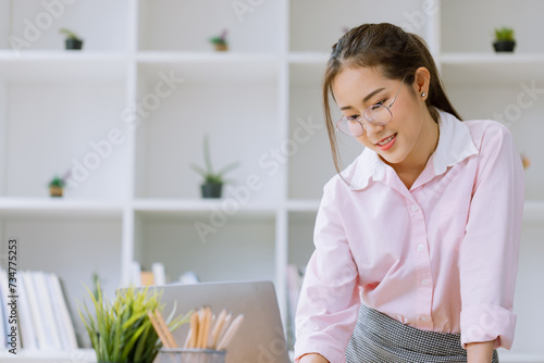 Happy asian young businesswoman using laptop with documents in office working space.