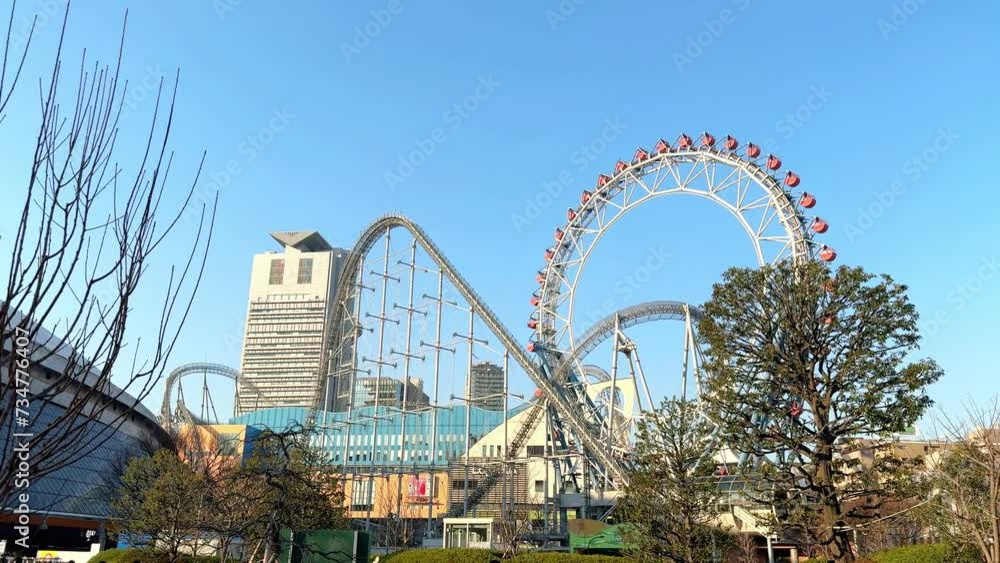 Skyline view of a Ferris wheel and roller coaster in an amusement park with city buildings in the background, clear day Skyline view of a Ferris wheel and roller coaster in an amusement park with city buildings in the background, clear day