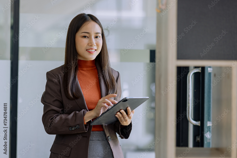 Happy asian young businesswoman using digital tablet standing in office office working space.