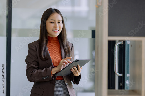 Happy asian young businesswoman using digital tablet standing in office office working space.