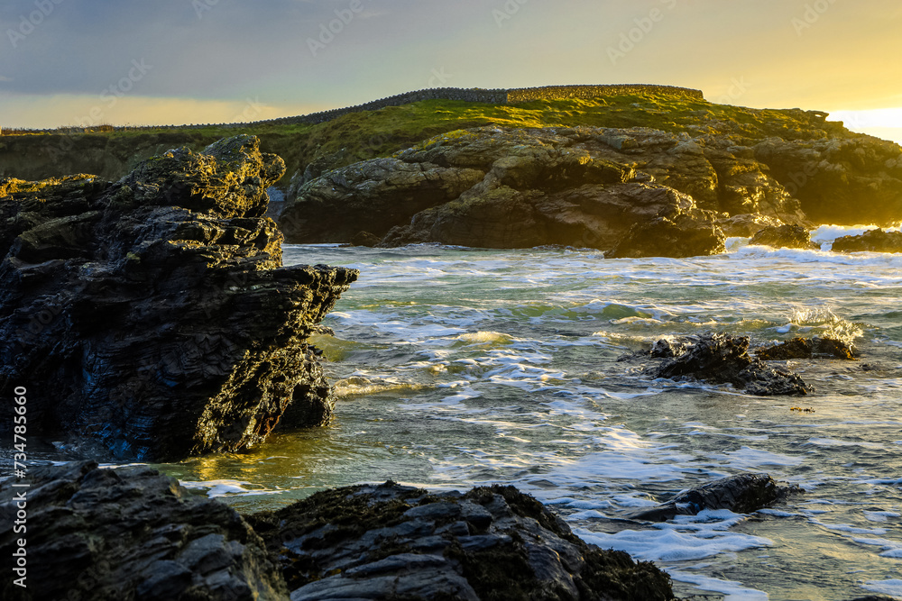 View of the serene ocean and rocky shoreline illuminated by golden sunlight