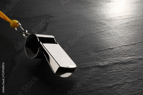 Referee equipment. Metal whistle on black textured background, closeup and space for text photo