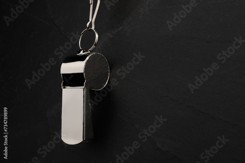 Referee equipment. Metal whistle on black textured background, closeup and space for text