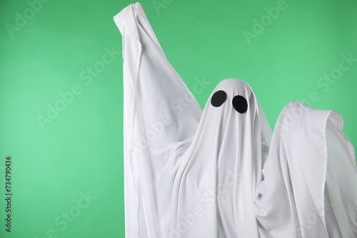 Creepy ghost. Person covered with white sheet on green background, space for text