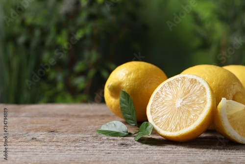 Fresh lemons and green leaves on wooden table outdoors, closeup. Space for text