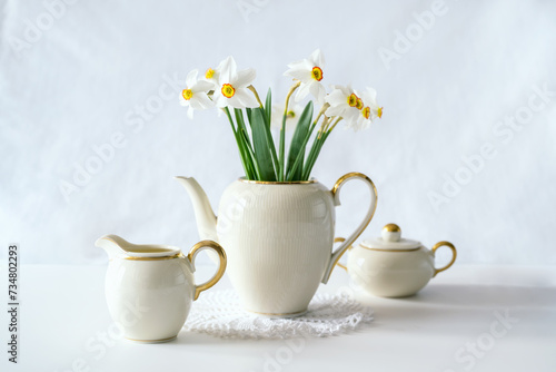 Fototapeta Naklejka Na Ścianę i Meble -  Still life with a blooming bouquet of white daffodils in an elegant porcelain teapot on a textured white background
