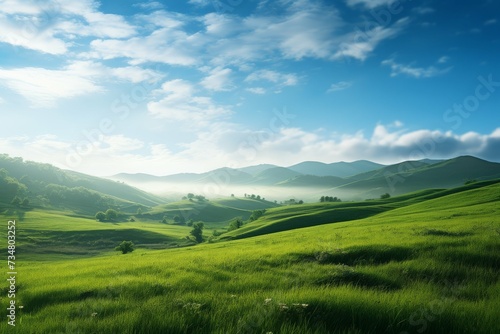 Rolling green hills under a clear blue sky with soft clouds at sunrise.