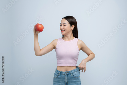 young woman show loose pants on waist after weightloss hold red apple isolated on white background