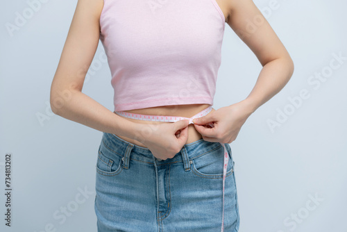 Cropped young woman in white clothes show loose pants after weightloss hold measure tape on waist