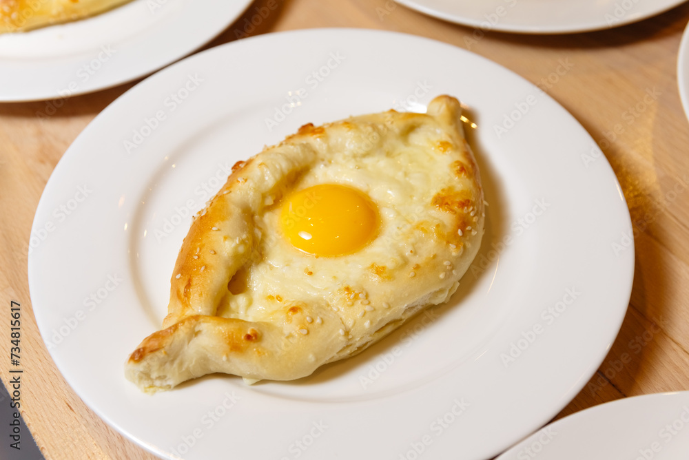 Adjarian Khachapuri with Egg on White Plate. Close-up of a single serving of Adjarian khachapuri, a Georgian cheese bread with a perfectly cooked sunny-side up egg in the center.