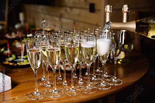 Champagne Service at a Cozy Event Gathering. A close-up view of champagne being poured into flutes, ready for a toast at an intimate social event with appetizers in the background.