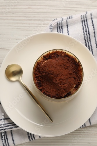 Delicious tiramisu in glass and spoon on white wooden table  top view